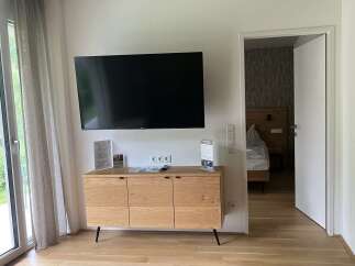 This is a bright and modern hotel room featuring a flat-screen TV mounted above a wooden cabinet.