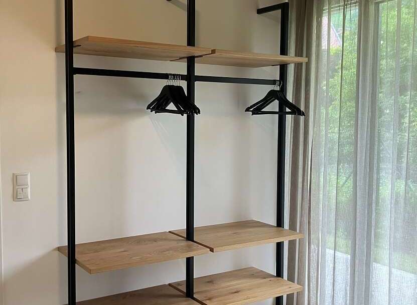 This modern bedroom features an open closet system with wooden shelves and black metal supports, providing ample storage and a minimalist aesthetic.