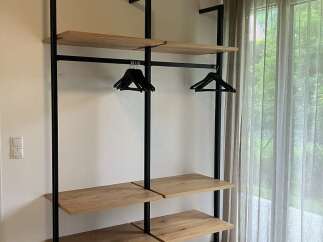 This modern bedroom features an open closet system with wooden shelves and black metal supports, providing ample storage and a minimalist aesthetic.