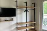 This property features a modern, open-concept closet design with sleek black metal framing and light wood shelving, offering both style and functionality.