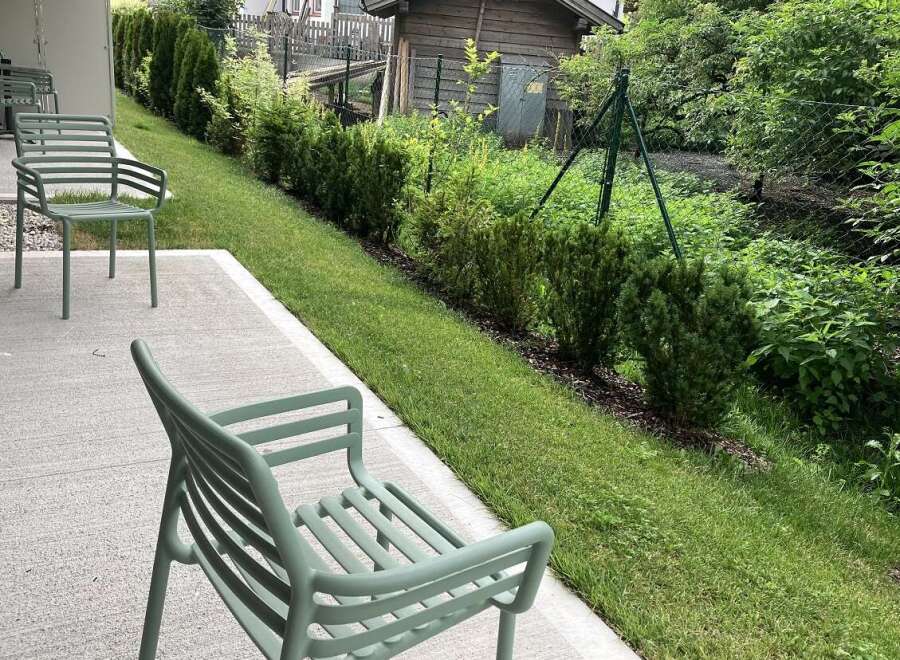 This outdoor patio space features minimalist green chairs, perfect for enjoying the well-maintained garden view.