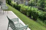 This outdoor patio space features minimalist green chairs, perfect for enjoying the well-maintained garden view.