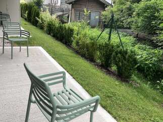 This outdoor patio space features minimalist green chairs, perfect for enjoying the well-maintained garden view.