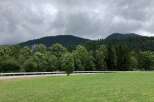 Discover a serene property with lush green fields, bordered by a quaint road and a backdrop of majestic mountains.