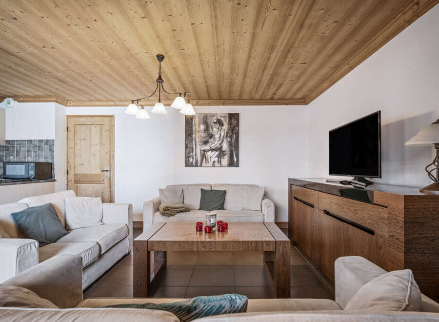 This cozy living room features a warm wood-paneled ceiling, comfortable sofas, and a modern entertainment center.