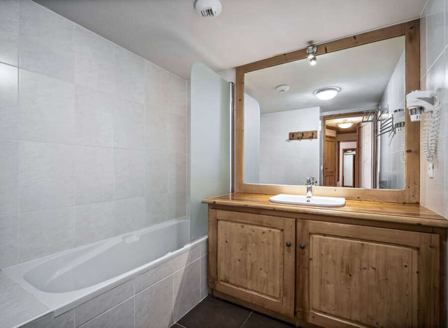 This bathroom features a bathtub with a glass partition and a wooden vanity with a sink and mirror.