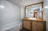 This bathroom features a bathtub with a glass partition and a wooden vanity with a sink and mirror.