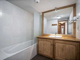 This bathroom features a bathtub with a glass partition and a wooden vanity with a sink and mirror.