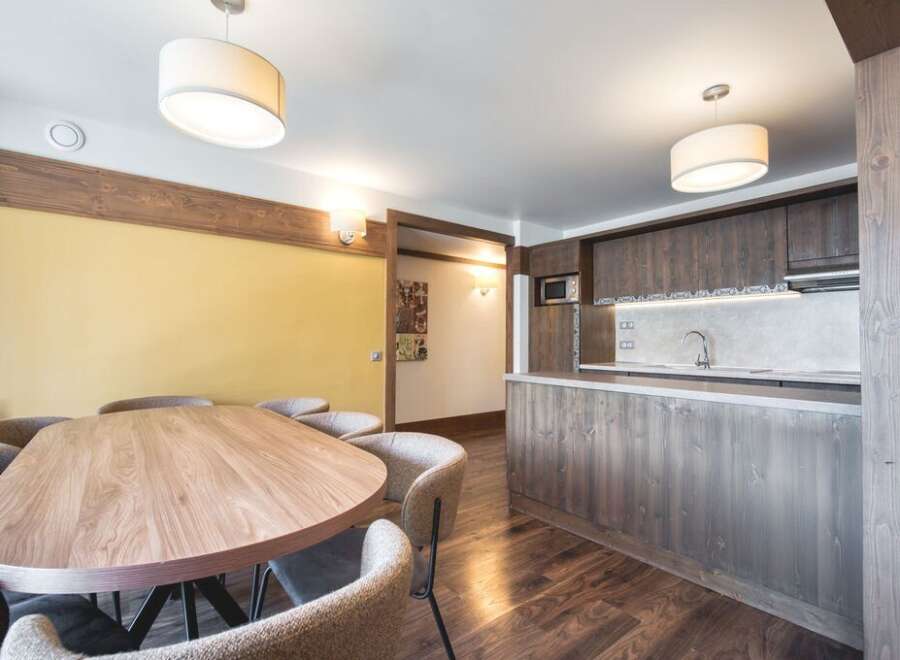 This inviting property features a spacious dining area with a large wooden table and comfortable seating, seamlessly flowing into a modern kitchen equipped with sleek wooden cabinetry and countertops.