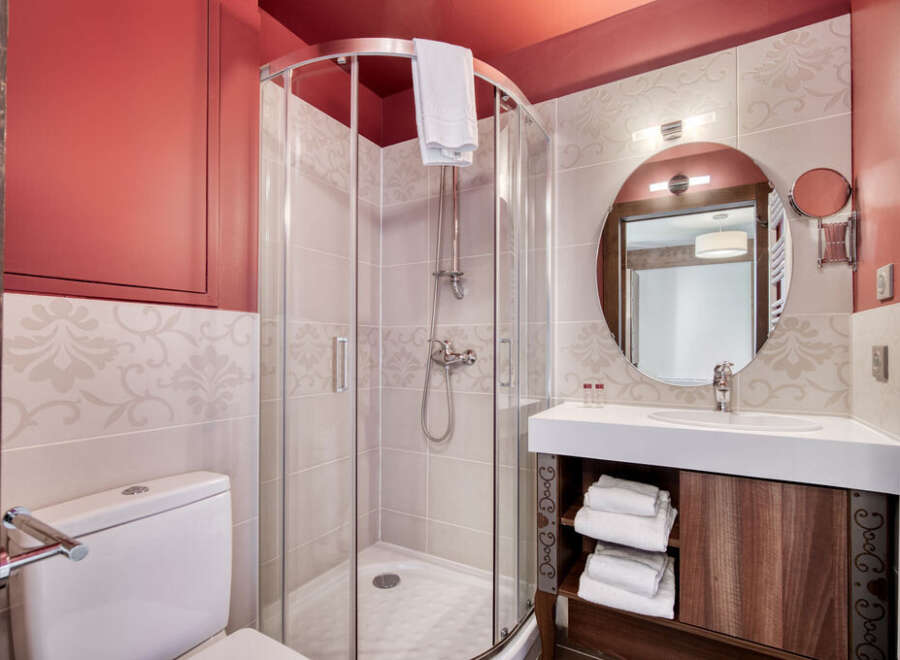 This bathroom features a modern shower with glass enclosure, a sleek vanity with ample storage, and a round mirror that enhances the space.
