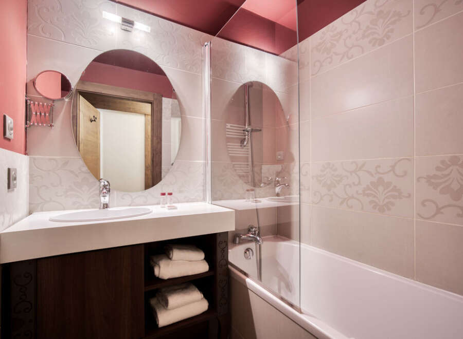 This charming bathroom features stylish floral-patterned tiles, a round mirror, and a sleek white countertop with a dark wood vanity.