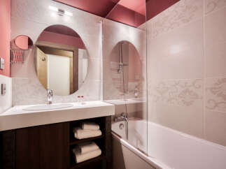 This charming bathroom features stylish floral-patterned tiles, a round mirror, and a sleek white countertop with a dark wood vanity.