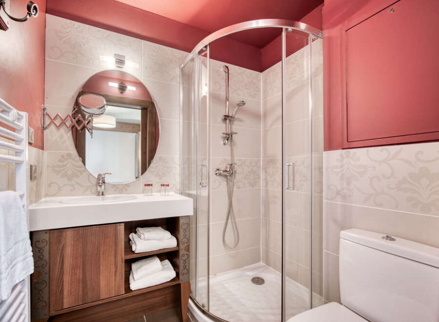 This well-lit bathroom features a modern design with a walk-in shower, a vanity with a round mirror, and a toilet.