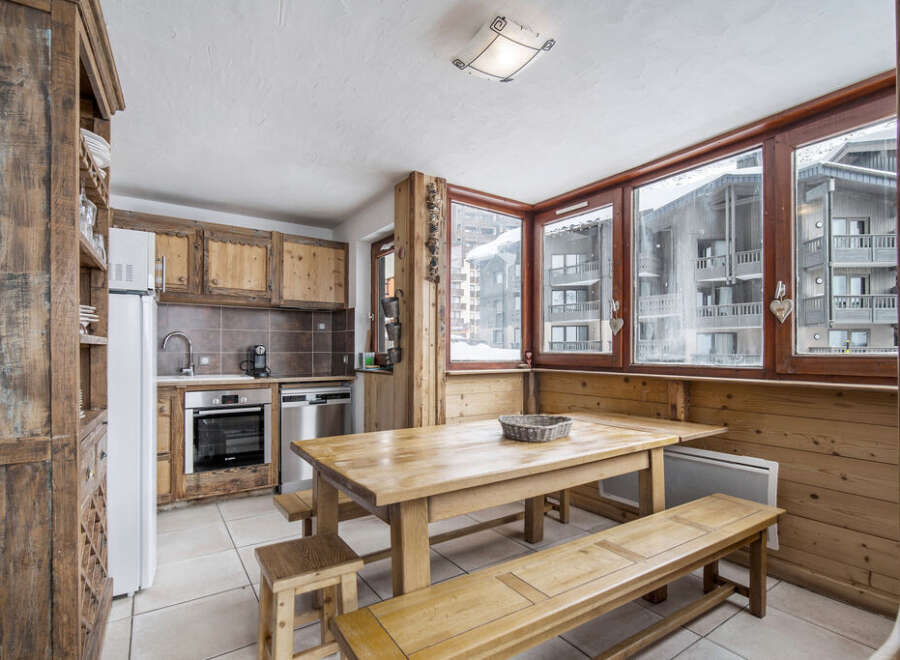 This charming kitchen features rustic wooden cabinetry, a spacious dining table with benches, and large windows offering picturesque views of the snowy landscape.