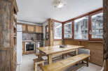 This charming kitchen features rustic wooden cabinetry, a spacious dining table with benches, and large windows offering picturesque views of the snowy landscape.