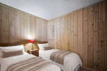 This charming bedroom features twin beds, natural wood paneling, and warm lighting, creating a cozy and inviting space.