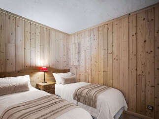 This charming bedroom features twin beds, natural wood paneling, and warm lighting, creating a cozy and inviting space.