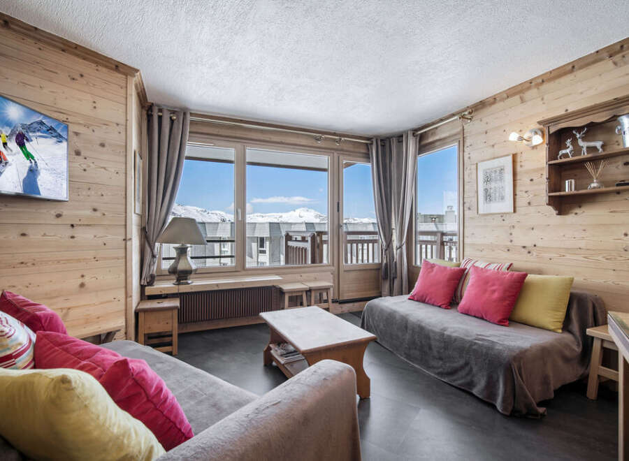 This cozy living room in a ski chalet features wood-paneled walls, comfortable seating, and large windows with stunning mountain views.