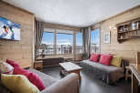 This cozy living room in a ski chalet features wood-paneled walls, comfortable seating, and large windows with stunning mountain views.