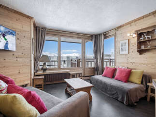 This cozy living room in a ski chalet features wood-paneled walls, comfortable seating, and large windows with stunning mountain views.