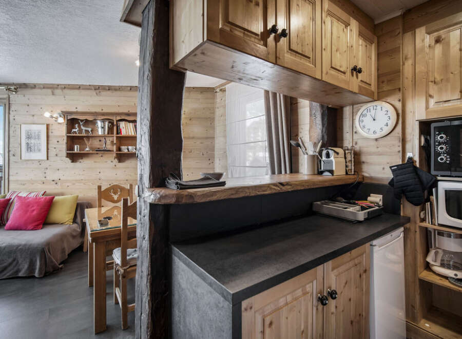 This charming property features a cozy living area with wood-paneled walls, seamlessly connected to a compact yet functional kitchen.