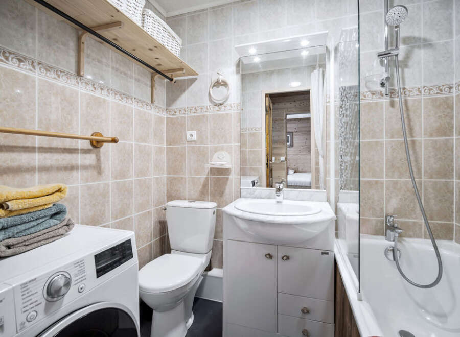 This bathroom features beige tile walls, a white vanity with marble countertop, and a shower-tub combo.