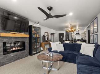 This inviting living room features a sleek fireplace with a stone surround and a rustic wooden mantel, complemented by a modern black ceiling fan.