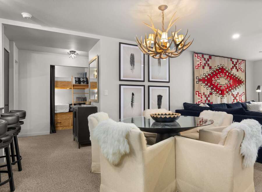 This stylish living space features a unique antler chandelier, a cozy dining area with fur-covered chairs, and a comfortable lounge area with a vibrant patterned rug.
