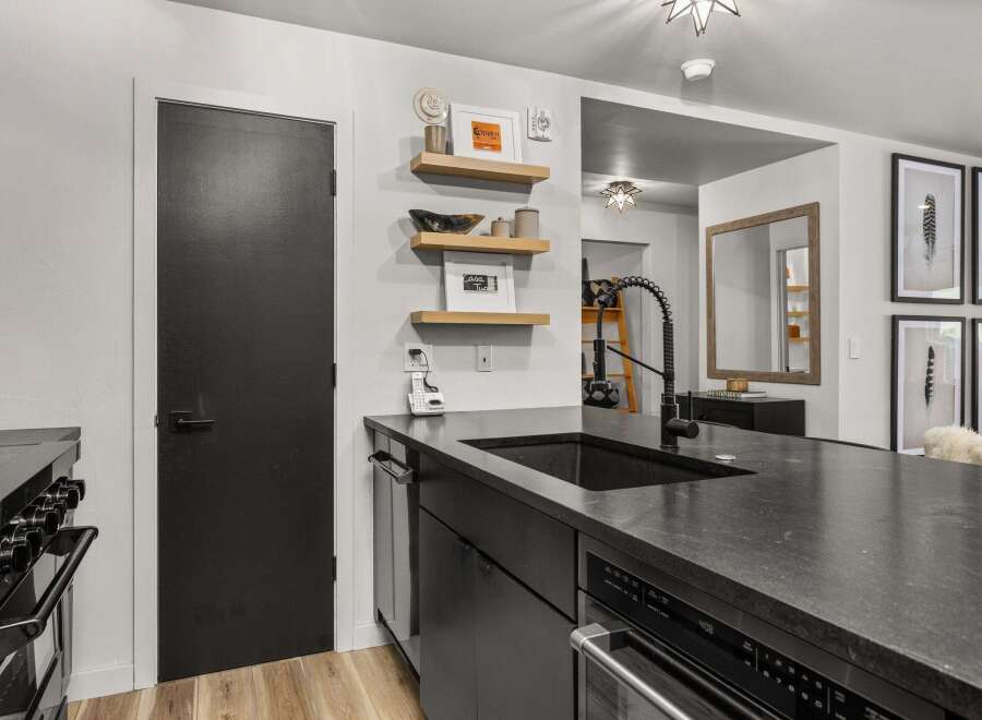 This modern kitchen boasts sleek black countertops and cabinetry, complemented by stylish wooden floating shelves.