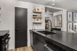 This modern kitchen boasts sleek black countertops and cabinetry, complemented by stylish wooden floating shelves.