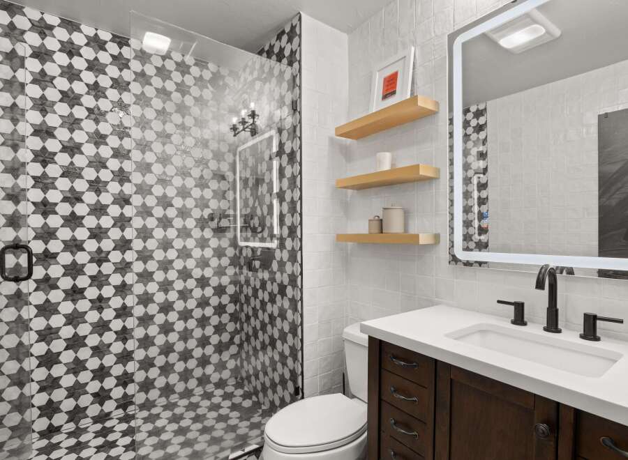 This bathroom features a modern design with a striking black and white patterned shower, complemented by a sleek vanity with a white countertop and dark wood cabinetry.