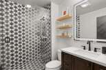 This bathroom features a modern design with a striking black and white patterned shower, complemented by a sleek vanity with a white countertop and dark wood cabinetry.