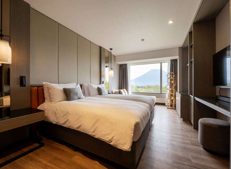 Indulge in the comfort of this hotel room featuring twin beds, a large window with scenic mountain views, and modern decor.