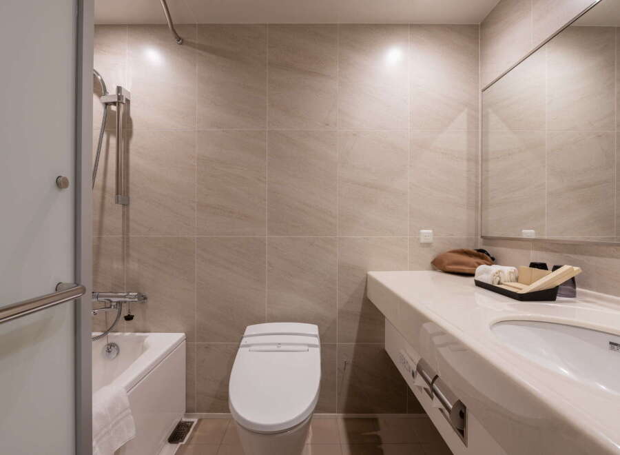 This modern bathroom features neutral beige tiling, a sleek bathtub with a shower, and a contemporary toilet.