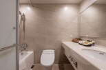 This modern bathroom features neutral beige tiling, a sleek bathtub with a shower, and a contemporary toilet.