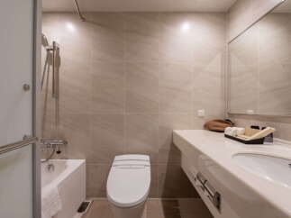 This modern bathroom features neutral beige tiling, a sleek bathtub with a shower, and a contemporary toilet.