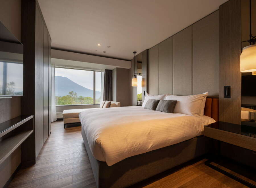 Experience ultimate comfort in this hotel room featuring a plush king-size bed, a cozy chaise lounge by the window, and stylish pendant lighting.