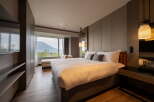 Experience ultimate comfort in this hotel room featuring a plush king-size bed, a cozy chaise lounge by the window, and stylish pendant lighting.