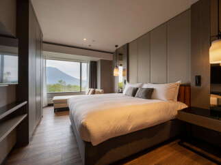 Experience ultimate comfort in this hotel room featuring a plush king-size bed, a cozy chaise lounge by the window, and stylish pendant lighting.