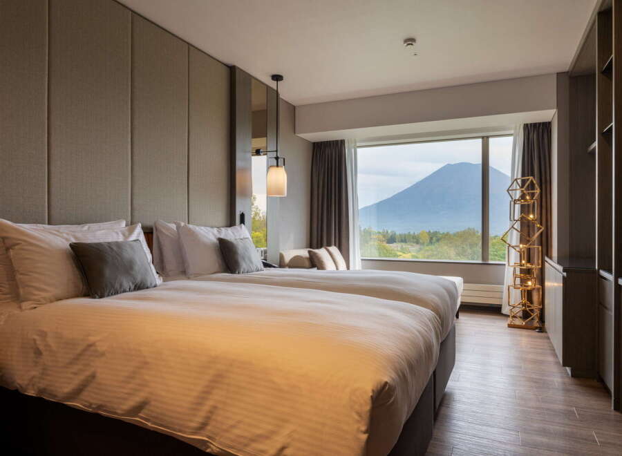 This hotel room offers a serene retreat with its plush double beds, stylish lighting, and a stunning view of the mountain.