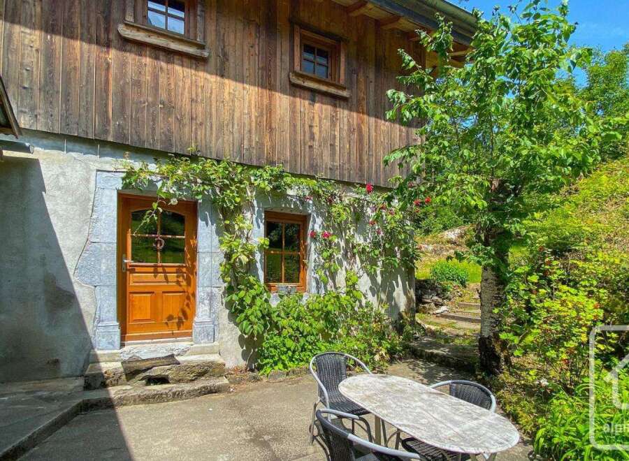 Charming chalet exterior featuring a stone foundation adorned with climbing vines and red roses, complemented by wooden cladding.