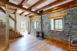 Discover this charming chalet featuring exposed wooden beams, a rustic stone wall, and a cozy wood-burning stove.