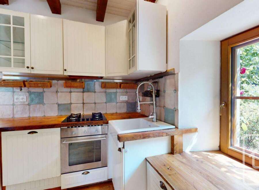 This charming kitchen features white cabinetry, a wooden countertop, and a rustic tiled backsplash.