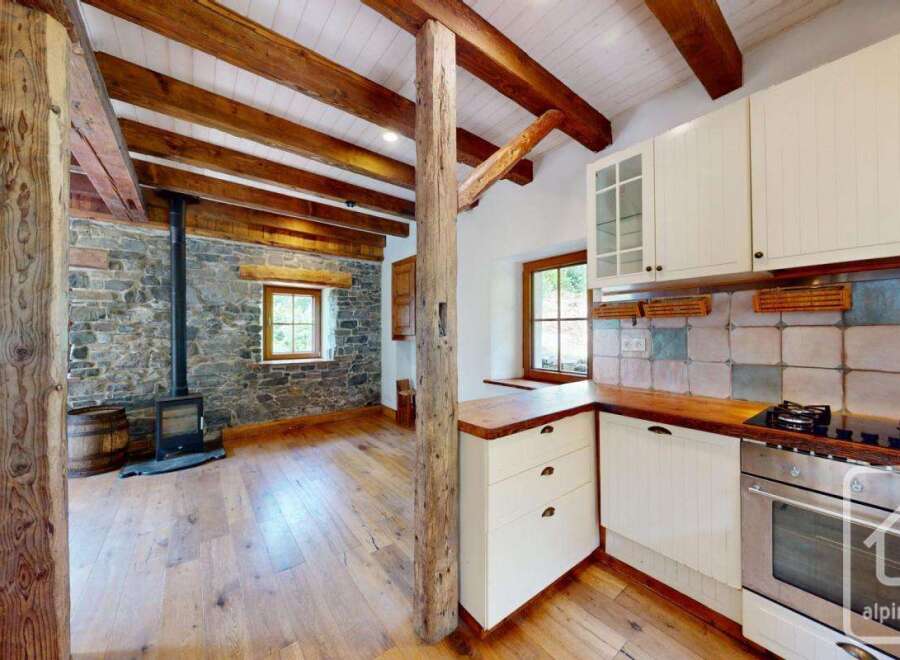 This property features a rustic interior with exposed wooden beams, a stone wall, and hardwood flooring.