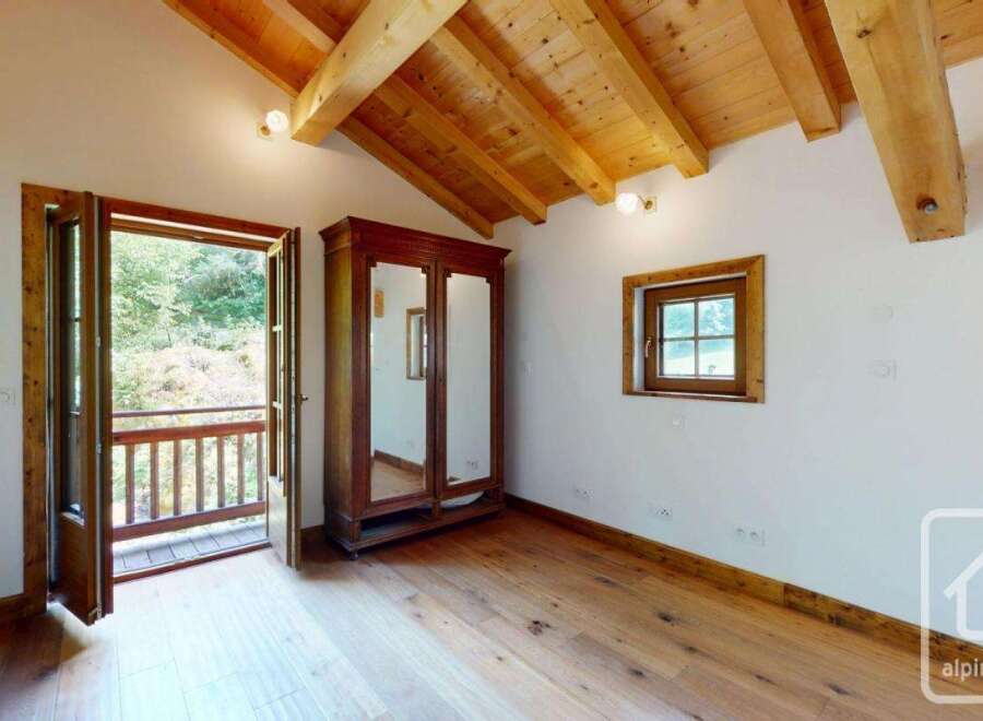 A bright bedroom features wooden flooring, a matching wooden ceiling with exposed beams, and a classic wardrobe with mirrored doors.