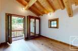 A bright bedroom features wooden flooring, a matching wooden ceiling with exposed beams, and a classic wardrobe with mirrored doors.