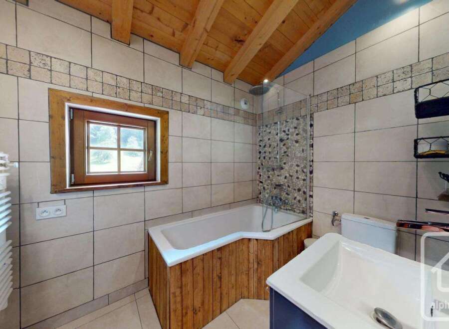This bathroom features a bathtub with wood paneling, a window bringing in natural light, and tiled walls with a decorative border.