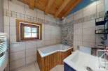 This bathroom features a bathtub with wood paneling, a window bringing in natural light, and tiled walls with a decorative border.