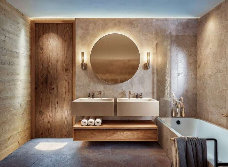 This modern bathroom features a sleek design with a floating double vanity, a round illuminated mirror, and a luxurious bathtub.
