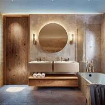 This modern bathroom features a sleek design with a floating double vanity, a round illuminated mirror, and a luxurious bathtub.